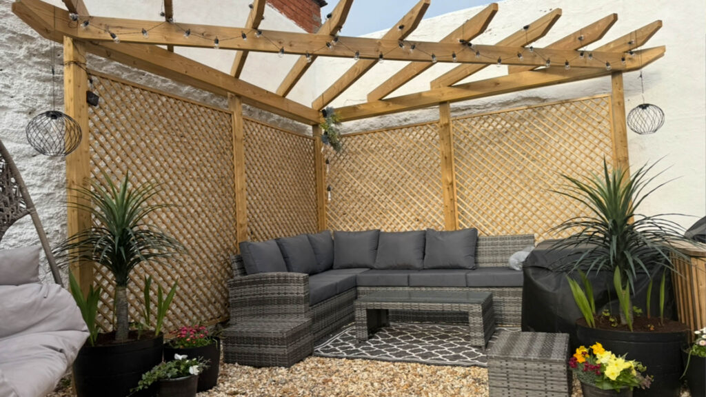 A wooden garden structure with garden sofa in the corner of the garden